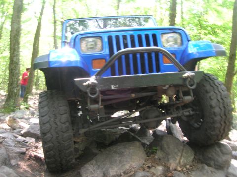 1996 Ford Bronco - A blue Jeep Wrangler navigates a rocky trail with its front end angled upwards.