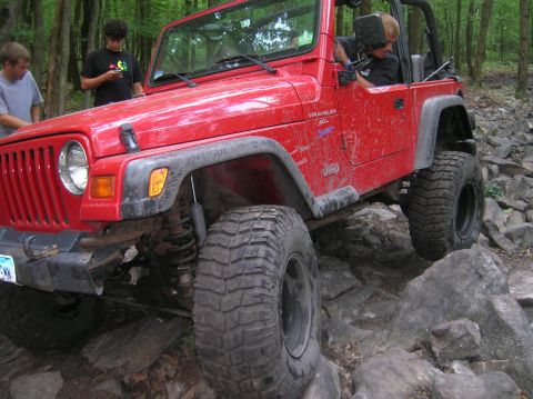 1996 Ford Bronco - A red Jeep Wrangler navigates a rocky trail with friends watching.
