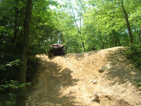 1996 Ford Bronco - An off-road vehicle navigates a steep, rocky incline amidst dense trees.