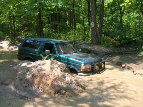 1996 Ford Bronco - A green 1996 Ford Bronco navigates a challenging muddy terrain on an off-road trail.