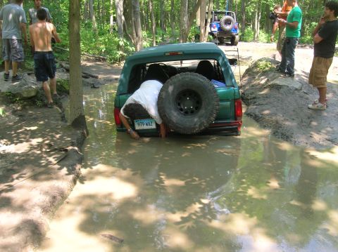 1996 Ford Bronco - A green 1996 Ford Bronco is stuck in a muddy puddle while onlookers watch.