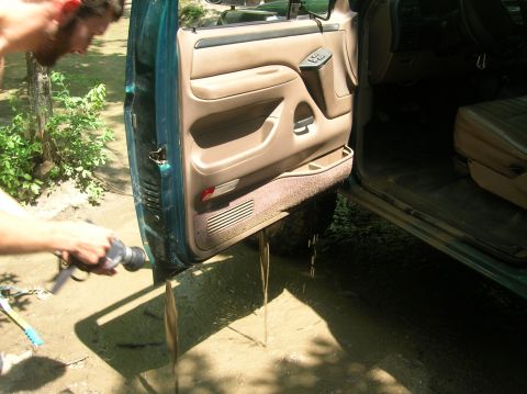 1996 Ford Bronco - Muddy water streams out from the door sill of a teal vehicle as someone washes it.