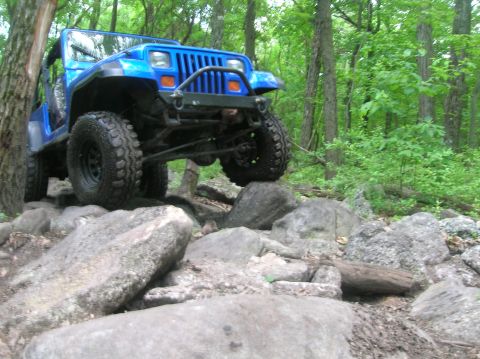 1996 Ford Bronco - A blue Jeep Wrangler is shown driving over large rocks on a wooded trail.