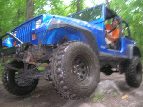 1996 Ford Bronco - A blue Jeep Wrangler navigates an off-road trail with a driver visible.