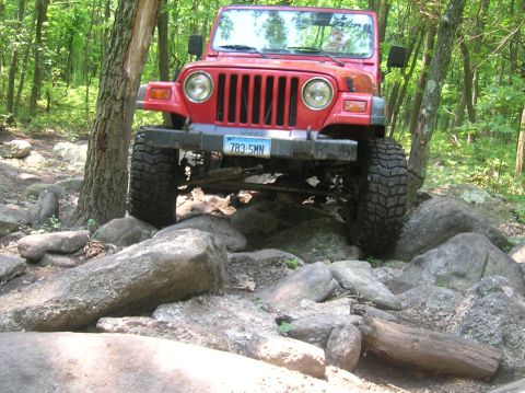 1996 Ford Bronco - A red Jeep Wrangler tackles a challenging rocky off-road course.