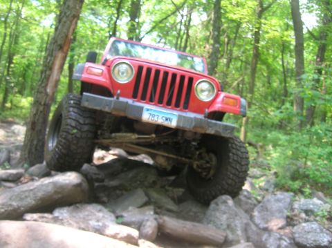 1996 Ford Bronco - Red Jeep Wrangler navigating a rocky off-road trail in a forest.