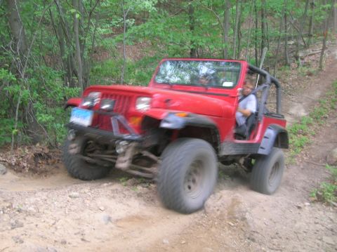 1996 Ford Bronco - A red Jeep Wrangler navigates a challenging off-road trail with a driver visible.