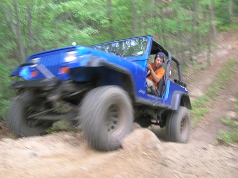 1996 Ford Bronco - A blue Jeep Wrangler navigates a rocky, off-road trail with a driver behind the wheel.