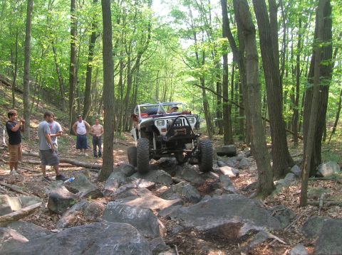 1996 Ford Bronco - A modified Jeep navigates a rocky trail through a dense forest with several onlookers.