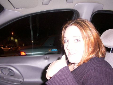 1998 Ford Taurus - A woman is inside a car at night, giving a thumbs up. A sticker is visible on the window.