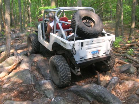 1996 Ford Bronco - A white off-road vehicle navigates a rocky trail in a wooded area.