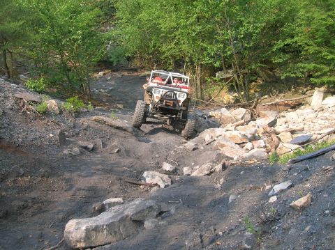 1996 Ford Bronco - An off-road vehicle navigates a challenging rocky trail surrounded by trees.