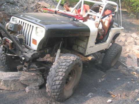 1996 Ford Bronco - Modified Jeep Wrangler navigating a rocky off-road trail with two occupants.