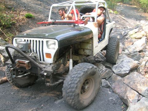 1996 Ford Bronco - A heavily modified Jeep Wrangler tackles a challenging rocky trail with two occupants.