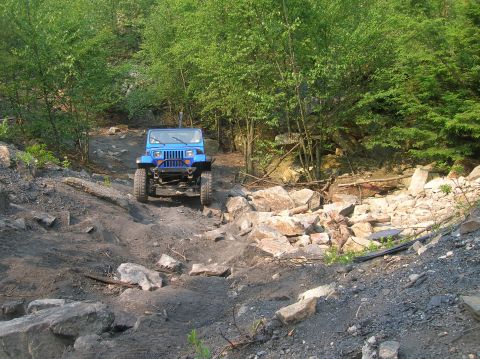 1996 Ford Bronco - A blue Jeep Wrangler tackles a challenging, rocky terrain on an off-road trail, demonstrating its off-road capabilities.