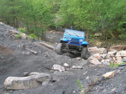 1996 Ford Bronco - Blue Jeep Wrangler navigating a challenging off-road course with rocky obstacles.