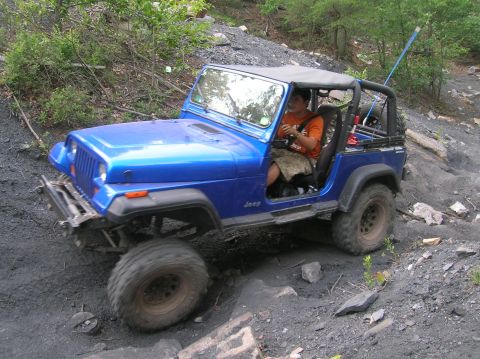 1996 Ford Bronco - A blue Jeep Wrangler navigates a challenging off-road course with a driver behind the wheel.