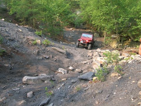 1996 Ford Bronco - Red Jeep Wrangler tackling a challenging off-road course on a sunny day.