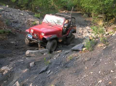 1996 Ford Bronco - A red Jeep Wrangler navigates a rocky off-road trail.