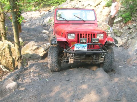 1996 Ford Bronco - A red Jeep Wrangler navigates a challenging rocky trail, demonstrating its off-road capabilities.