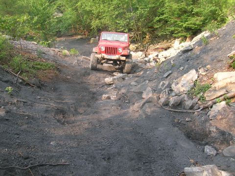 1996 Ford Bronco - Red Jeep Wrangler tackling a challenging, rocky off-road path.