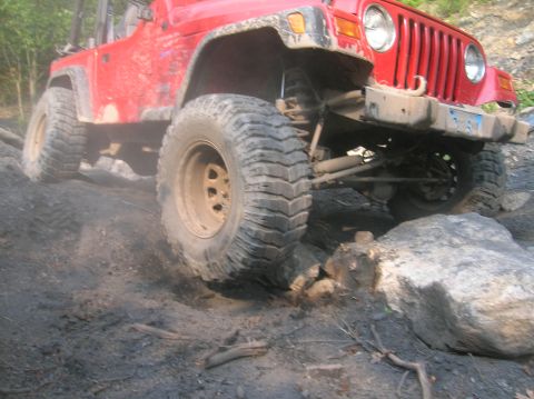 1996 Ford Bronco - A red Jeep Wrangler tackles a challenging off-road course with large tires and a lifted suspension.