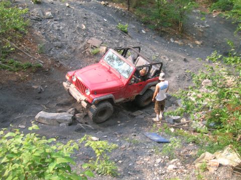 1996 Ford Bronco - A red Jeep Wrangler tackles a challenging off-road course with a driver and passenger inside.