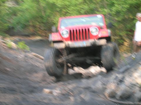 1996 Ford Bronco - Red Jeep Wrangler navigates a challenging off-road course with muddy terrain and rocks.