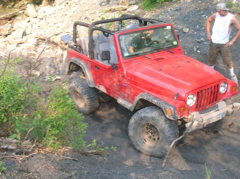 1996 Ford Bronco - A red Jeep Wrangler navigates an off-road trail with a person observing.