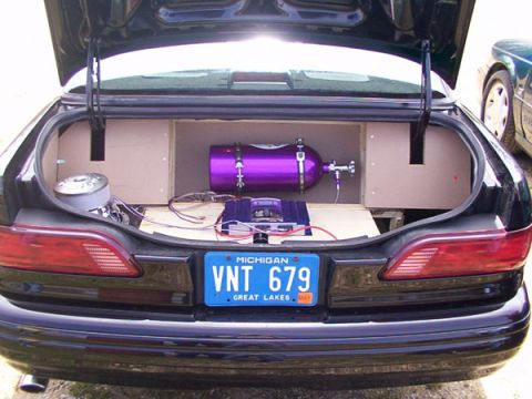 1998 Ford Taurus - The trunk of a car is open, revealing a purple nitrous oxide tank and an audio amplifier, with a Michigan license plate visible.