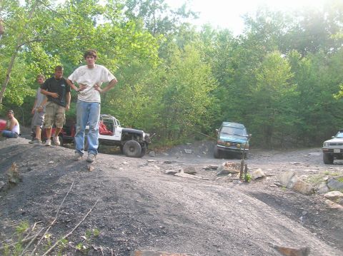 1996 Ford Bronco - Several off-road vehicles and people are gathered on a dirt path surrounded by trees.