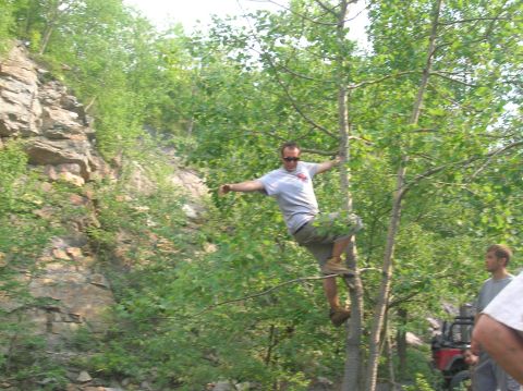 1996 Ford Bronco - Man climbs tree in wooded area with off-road vehicles nearby.