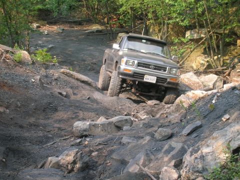 1996 Ford Bronco - A modified Toyota pickup truck tackles a challenging rocky incline on an off-road trail.