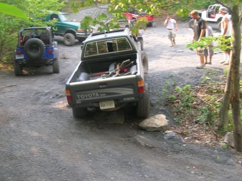 1996 Ford Bronco - Several off-road vehicles are parked on a gravelly path in a wooded area.