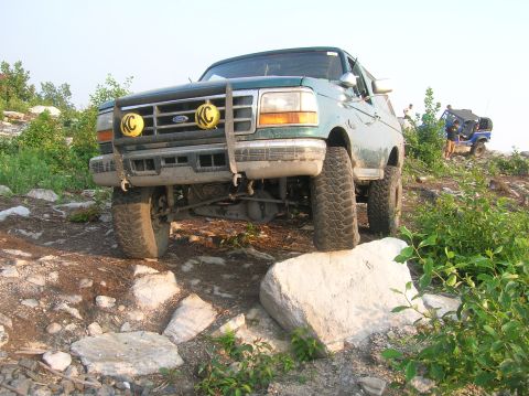 1996 Ford Bronco - A green Ford Bronco navigates a rocky terrain, with another off-road vehicle visible in the distance.