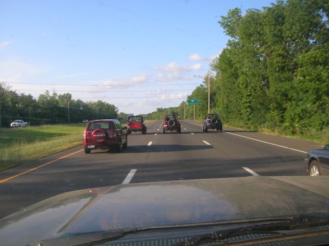 1996 Ford Bronco - A convoy of SUVs travels down a highway on a sunny day, with trees lining the road.