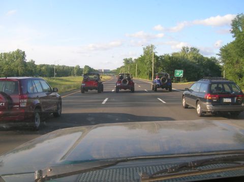 1996 Ford Bronco - Several Jeeps drive down a highway, with other vehicles in view.