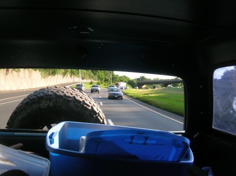 1996 Ford Bronco - View from inside a vehicle, showing a spare tire and cooler, with other cars on the highway ahead.