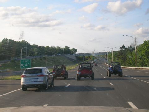 1996 Ford Bronco - A convoy of Jeeps travels down the highway under a partly cloudy sky, with an exit sign for route 43 in view.