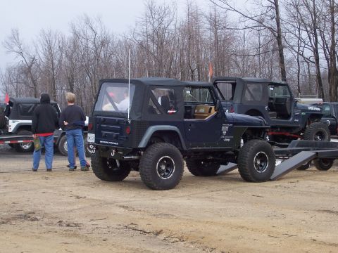 1996 Ford Bronco - Several modified Jeep Wranglers are parked outdoors on a dirt lot with trees in the background.
