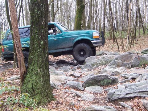 1996 Ford Bronco - A 1996 Ford Bronco tackles a challenging rocky path through a dense forest.