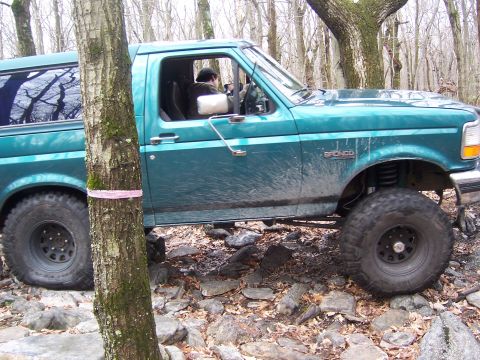 1996 Ford Bronco - A teal 1996 Ford Bronco navigates a rocky trail in a wooded area.