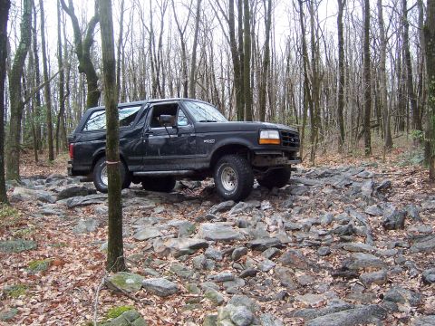 1996 Ford Bronco - 1996 Ford Bronco navigating a challenging rocky trail in a forest.