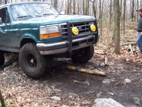 1996 Ford Bronco - A green 1996 Ford Bronco navigates rough terrain in a wooded area.