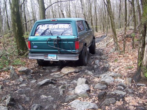 1996 Ford Bronco - 1996 Ford Bronco navigates a challenging rocky path through a dense forest.