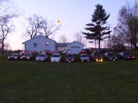 1998 Ford Taurus - Several sedans are parked on a grassy incline in front of a residential building.