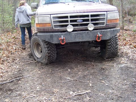 1996 Ford Bronco - A person stands next to a Ford Bronco with an aftermarket bumper and off-road tires in a wooded area.