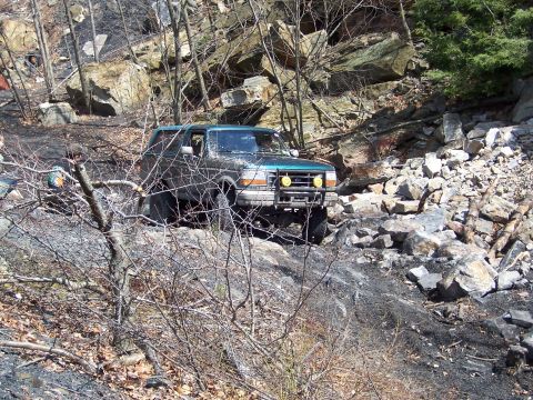 1996 Ford Bronco - A green Ford Bronco navigates a challenging off-road course with steep, rocky inclines and dense vegetation.