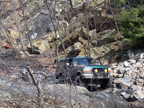 1996 Ford Bronco - A green 1996 Ford Bronco navigates a challenging rocky path in a wooded area.