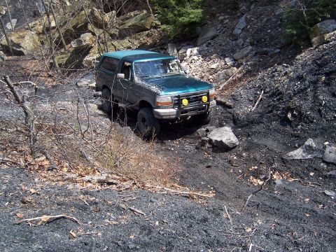1996 Ford Bronco - A green Ford Bronco navigates a challenging off-road path with steep, rocky terrain.